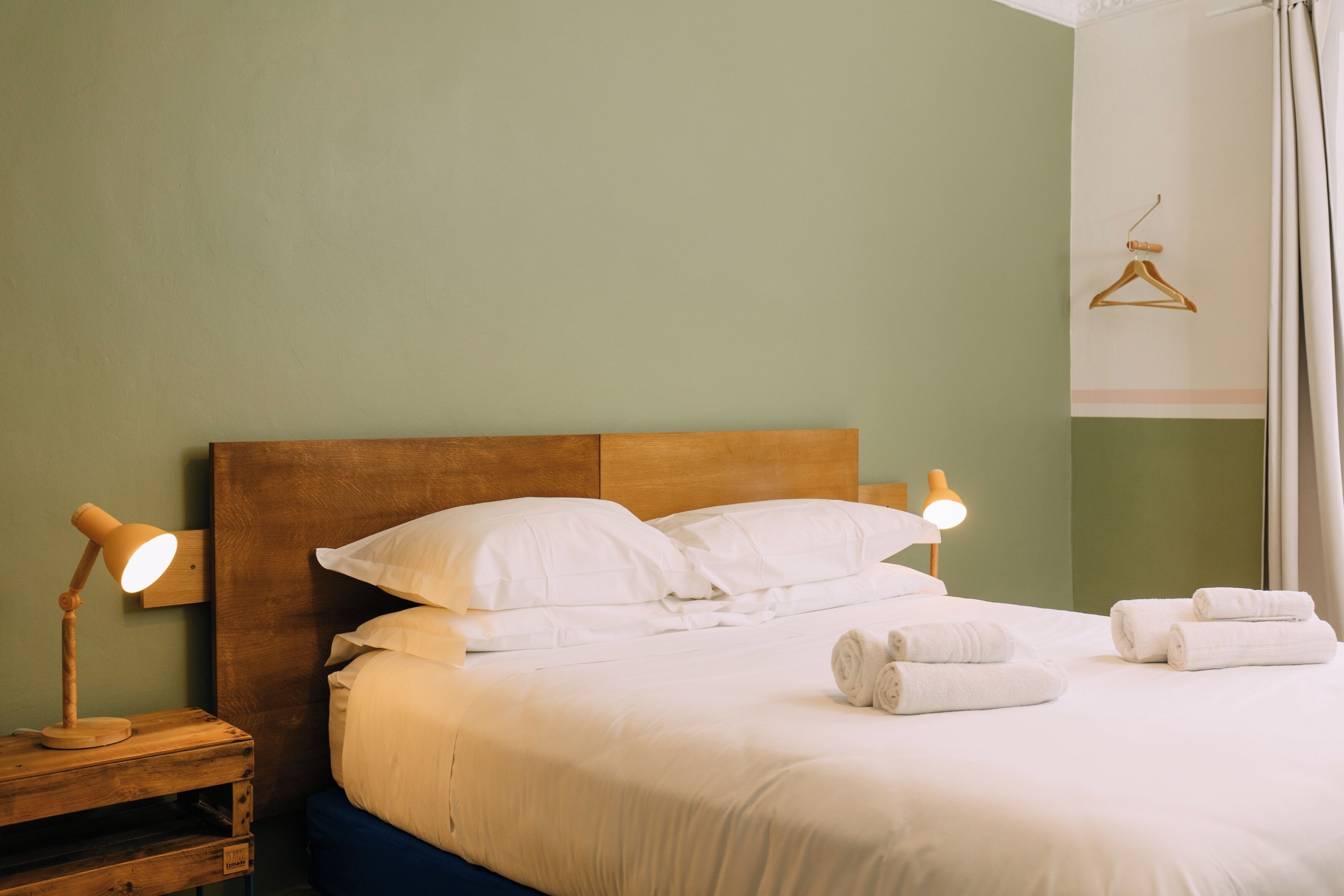 Una cama bien hecha con sábanas blancas, dos lámparas de noche y una mesita de madera.