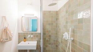 A bathroom with a white sink, a mirror, and a shower with green tiles. - Tomato Urban Retreat (Turin)