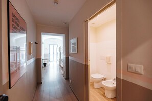 A hallway leading to a bathroom with a toilet and bidet, wooden flooring, and a framed picture on the wall. - Tomato Urban Retreat (Turin)