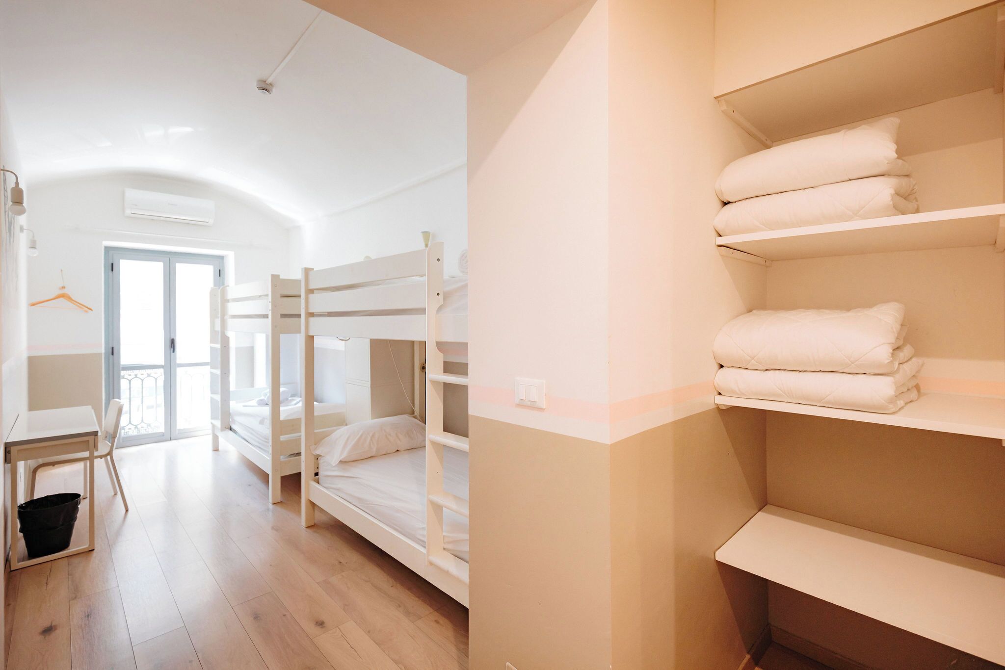 A room with bunk beds, a desk, and shelves with folded towels.