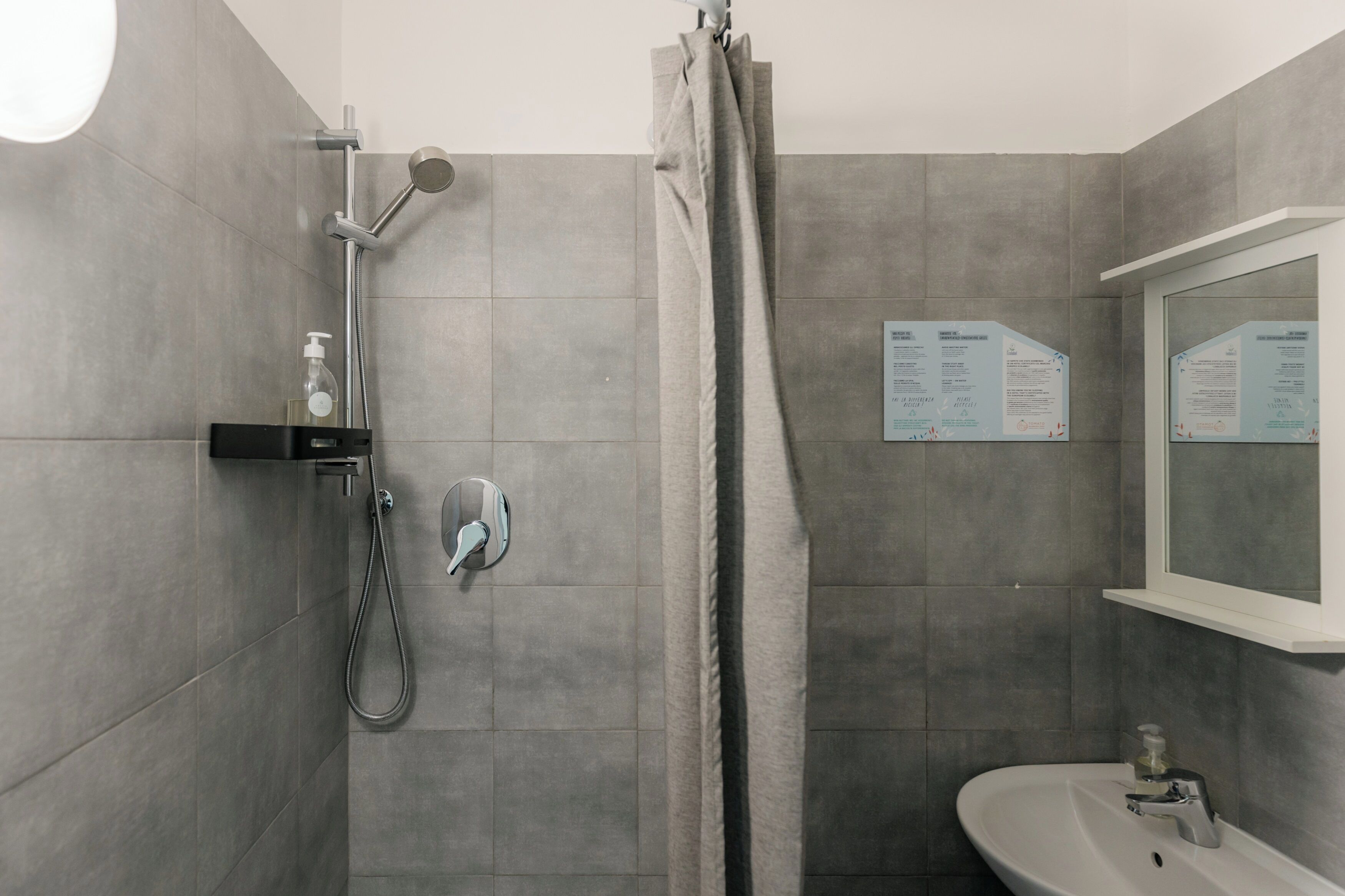 Un baño moderno con baldosas grises, ducha con cabezal de ducha manual, lavabo con espejo y toallero.