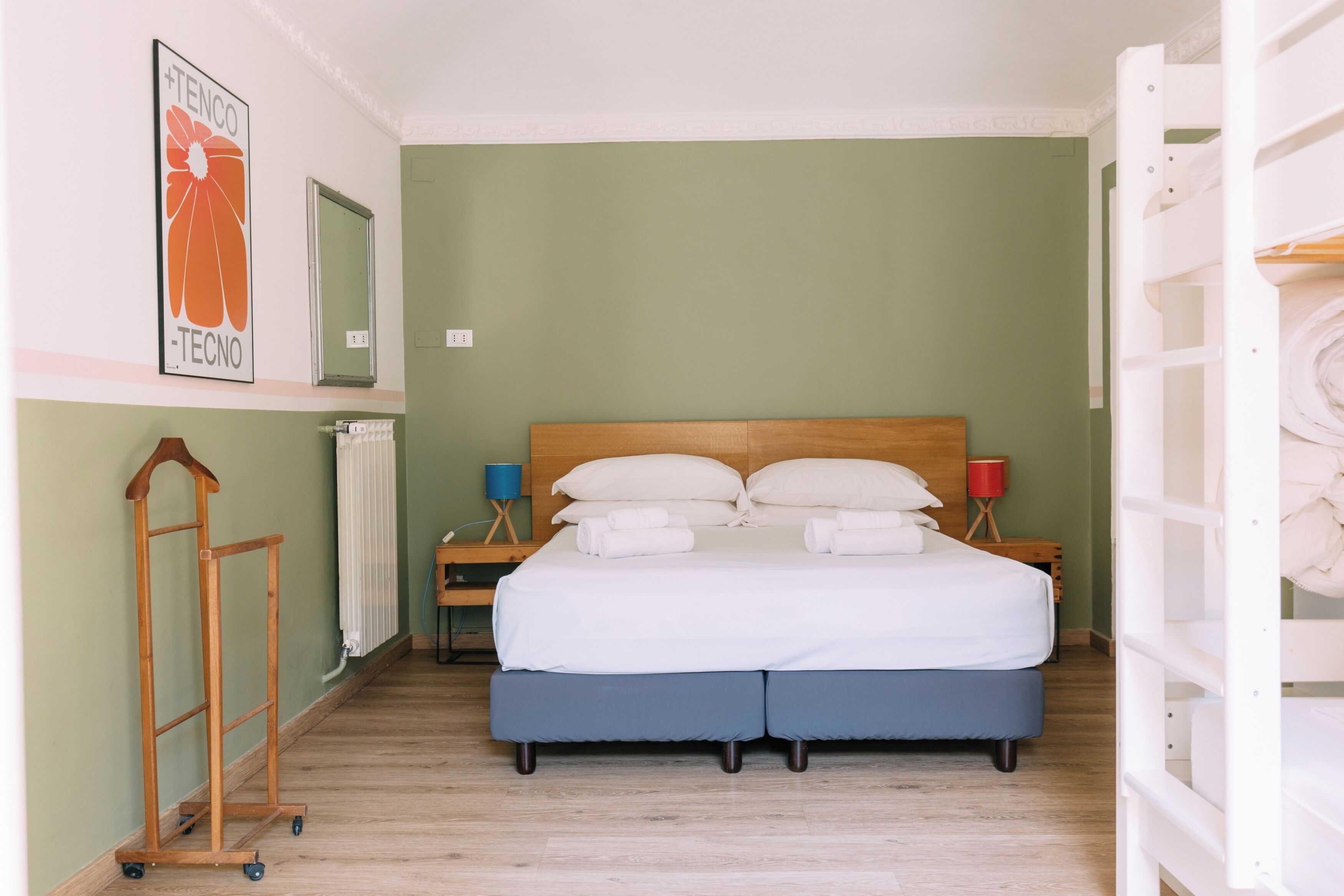 Un dormitorio con cama, mesitas de noche, radiador, suelo de madera e imagen colgada en la pared.