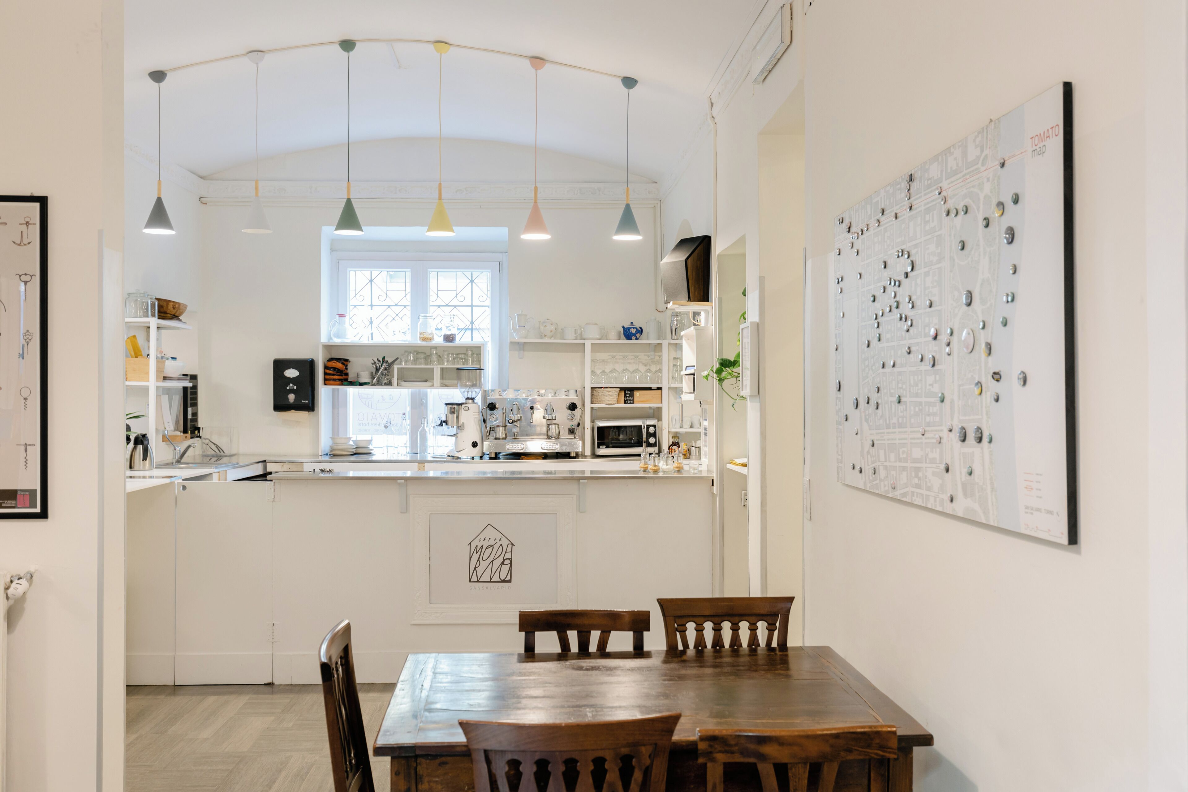 Une cuisine moderne avec des meubles blancs, un îlot central, des luminaires suspendus et un coin repas avec des chaises en bois.