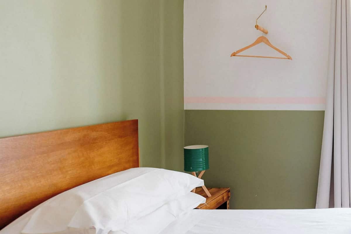 A neatly made bed with white linens, a wooden headboard, and a green cylindrical object on the nightstand.