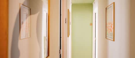 A hallway with framed pictures on the walls, a wooden floor, and a green wall at the end.