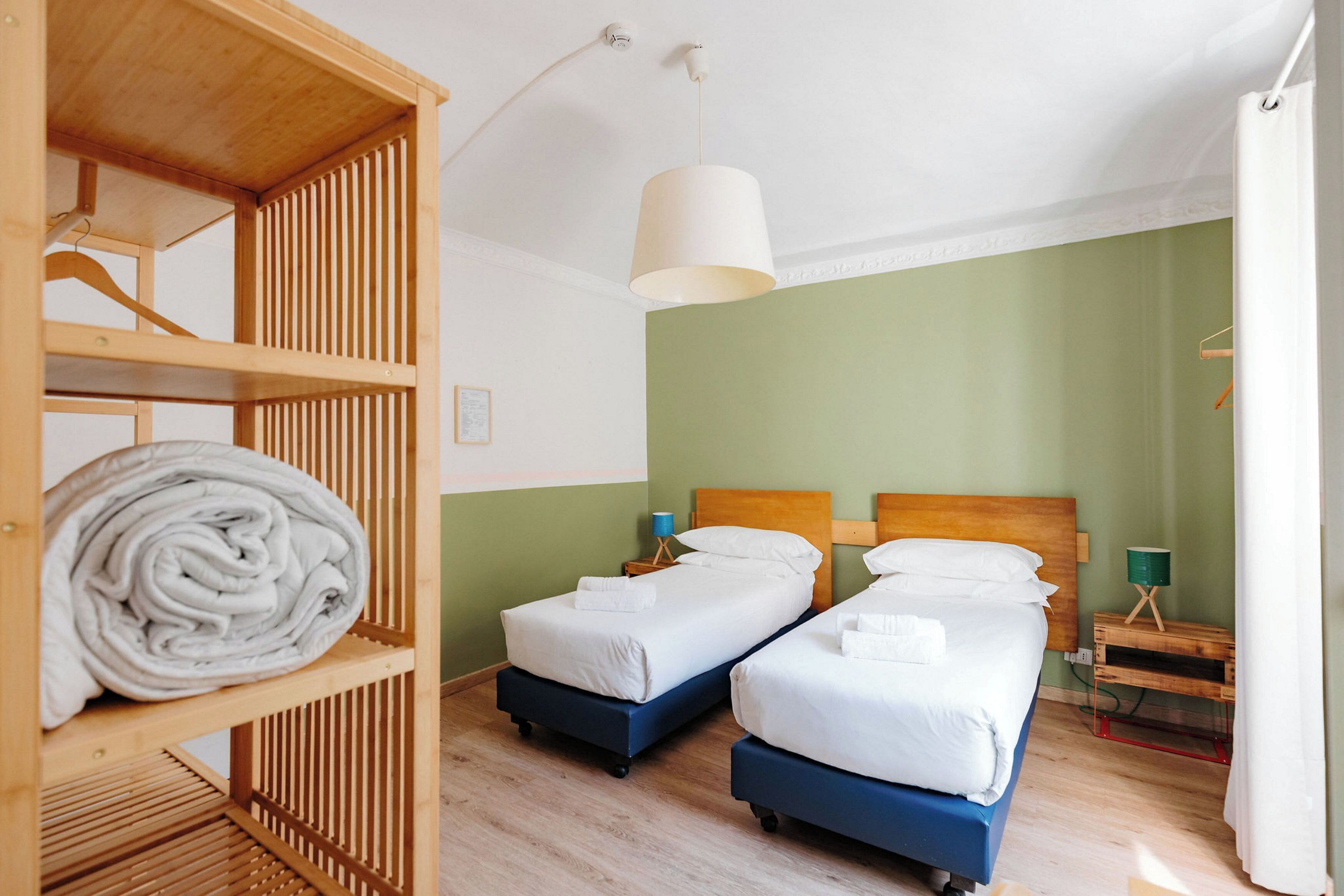 Quarto com duas camas, um guarda-roupa de madeira e um candeeiro pendente.