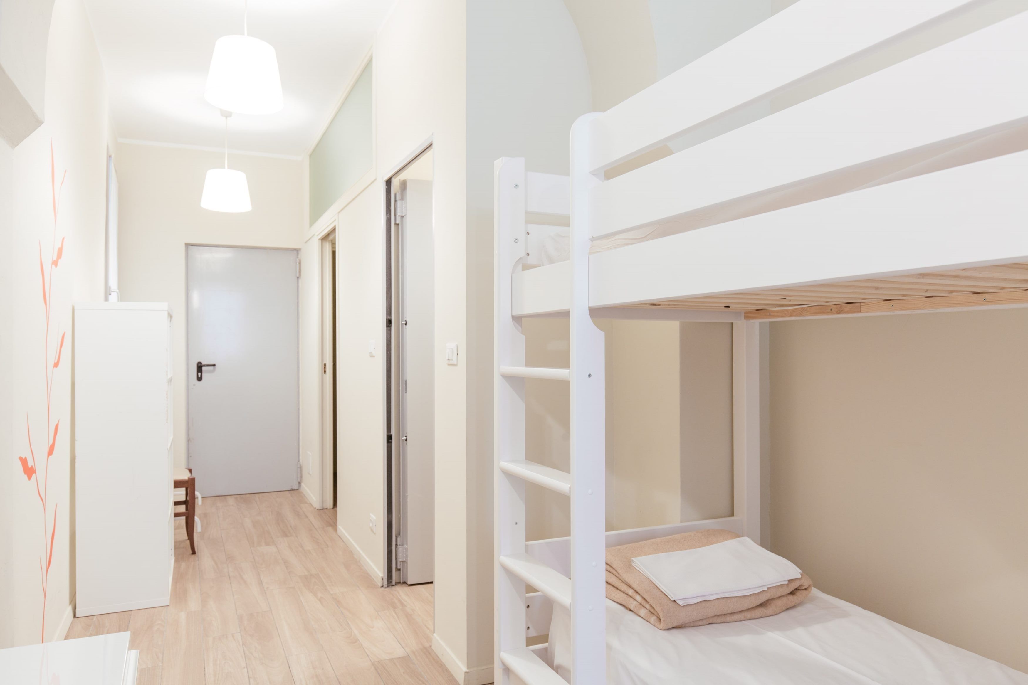 A room with bunk beds, a white door, a small table, and a hanging light fixture.