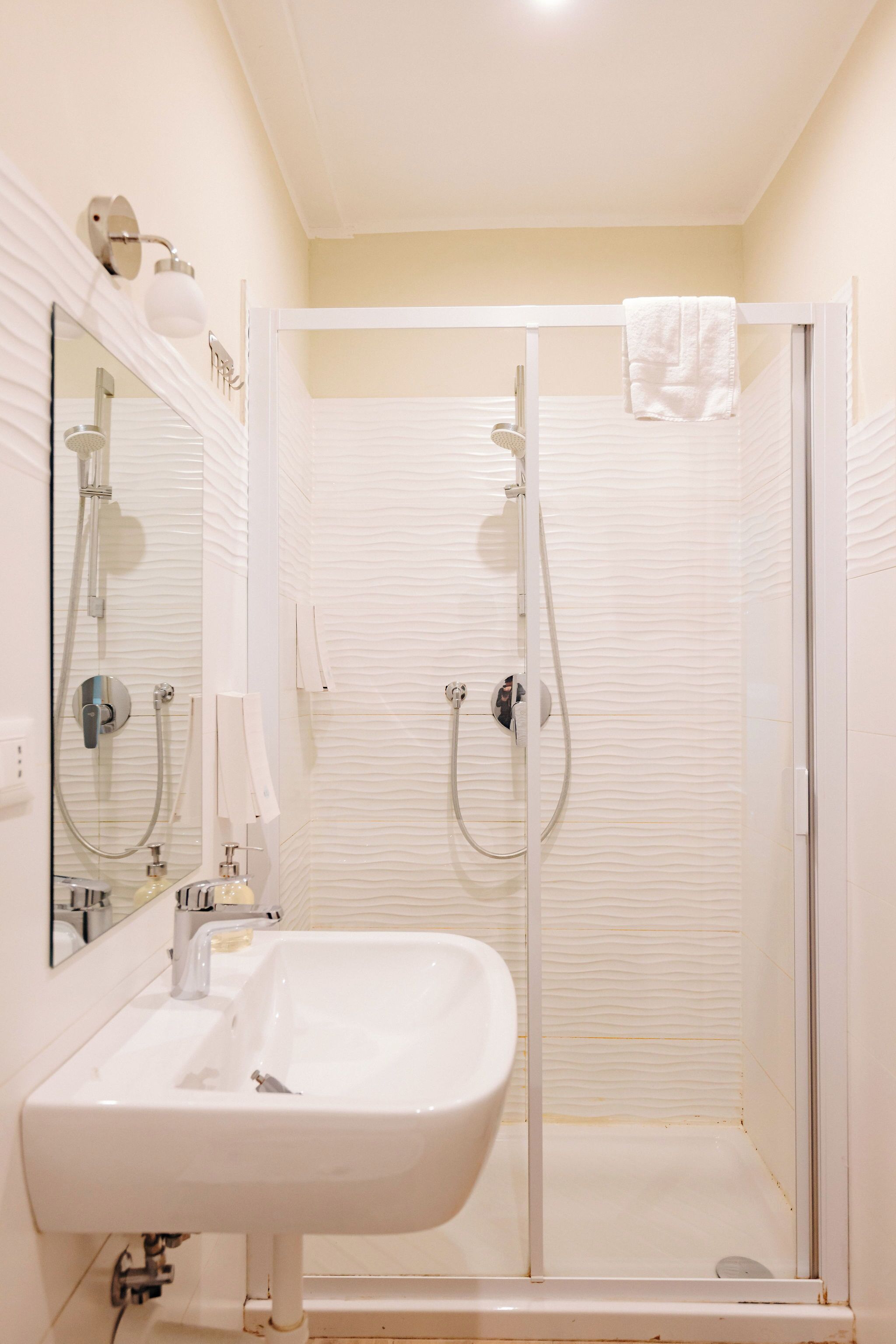 A bathroom with a white sink, a mirror, a shower enclosure, and a towel hanging on the shower door.