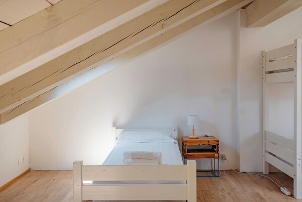 A small, single-bed room with a sloped ceiling, a wooden nightstand with a lamp, and a white bed.