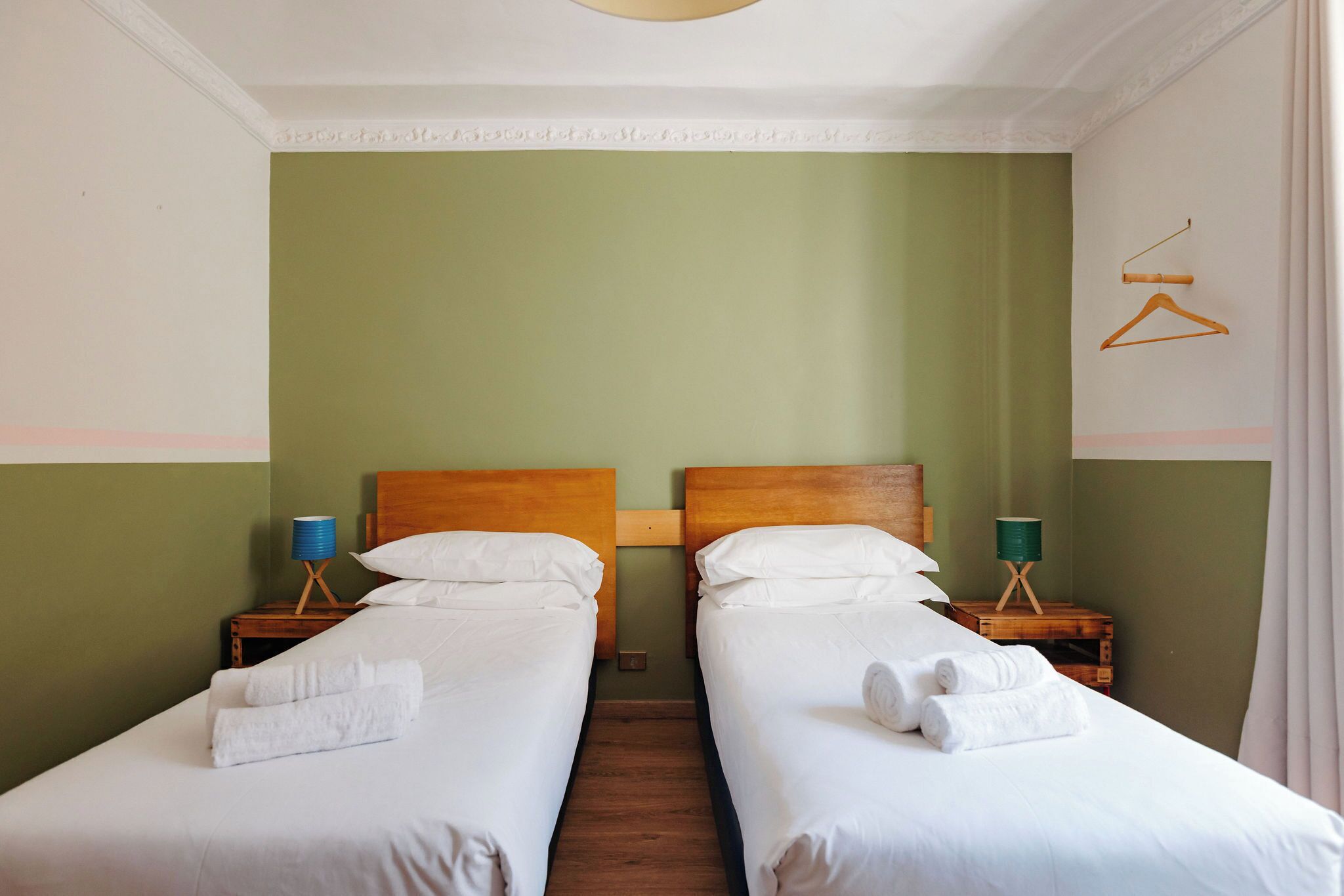 A double room with two beds, each with white linens and towels, wooden headboards, and bedside tables with lamps.