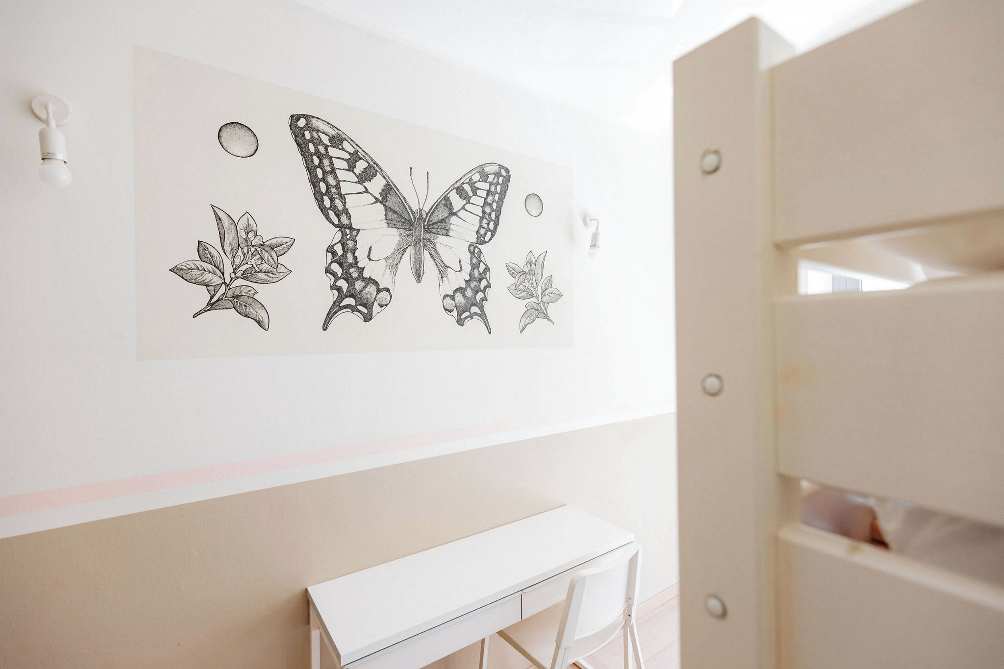 Una habitación con un escritorio blanco, una silla blanca y una obra de arte en la pared con una mariposa y hojas.