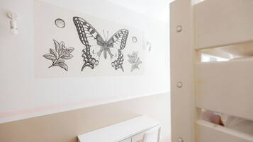 Una habitación con un escritorio blanco, una silla blanca y una obra de arte en la pared con una mariposa y hojas.