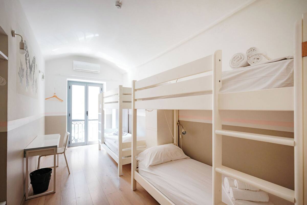A bunk bed room with a desk and chair, a hanging coat rack, and a door leading outside.
