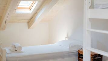 Une chambre avec un puits de lumière, un lit recouvert de draps blancs et une table de chevet en bois.