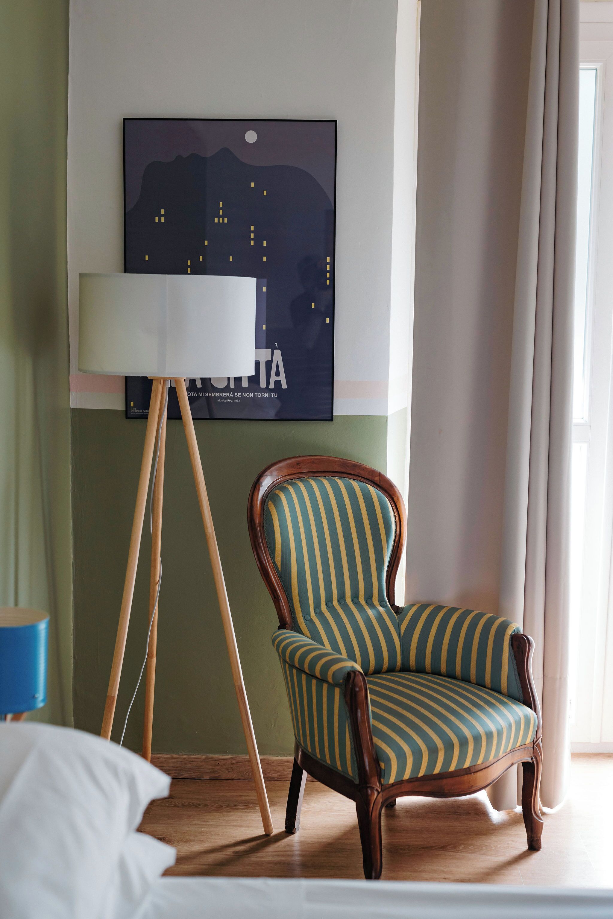 Quarto com piso de madeira, poltrona listrada, abajur e quadro emoldurado na parede.