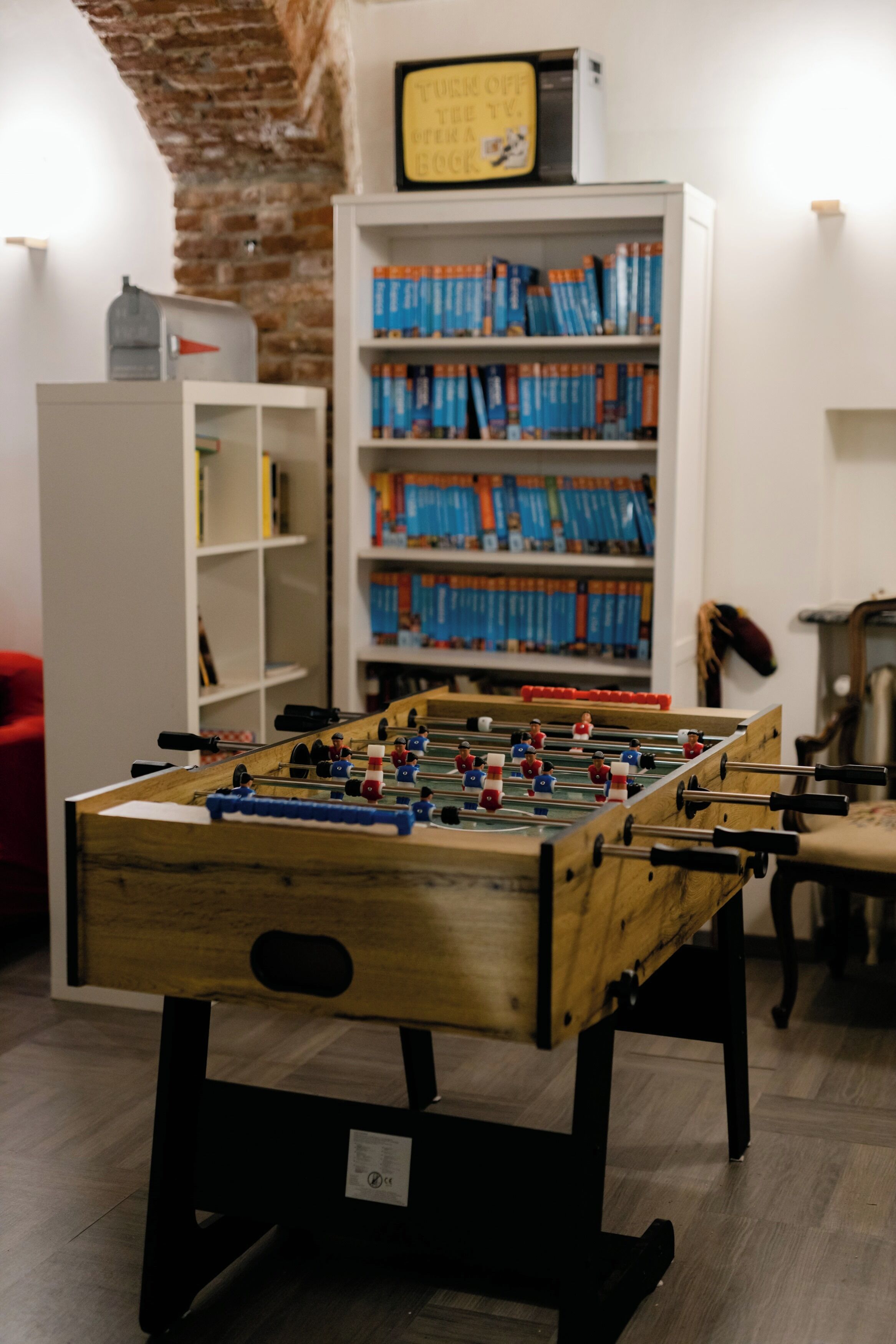 A foosball table in a room with a brick wall and a bookshelf filled with books.