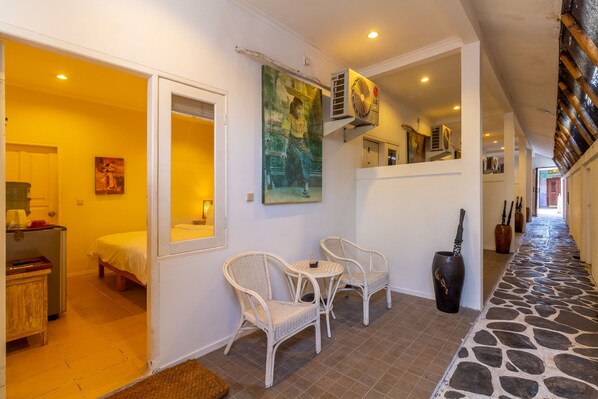 A hallway with wicker chairs, a painting, and a stone-tiled floor.