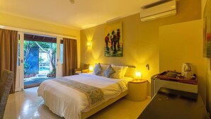 A hotel room with a bed, bedside tables, a painting, and a view of the outdoors. - Scallywags Mango (Gili Air)