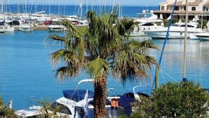 Un puerto deportivo con varias embarcaciones amarradas, palmeras y un edificio con tejado de baldosas al fondo.