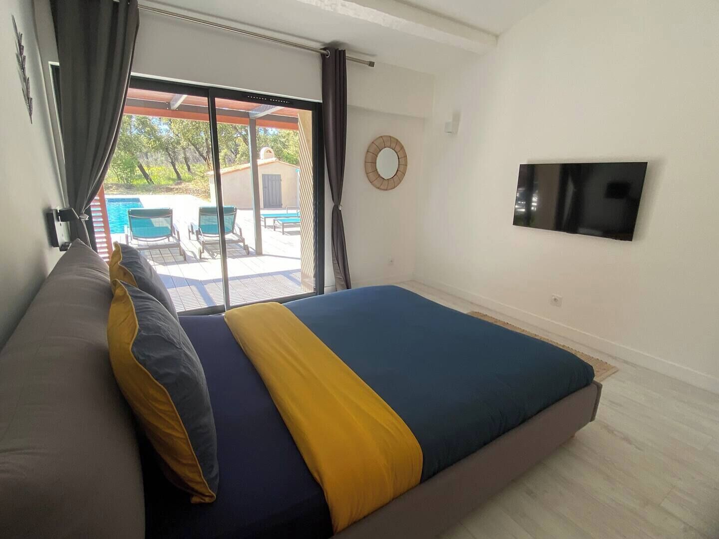 Ein Schlafzimmer mit Bett, Fernseher und Blick auf einen Außenpool sowie einer Schiebetür.