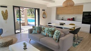 Una sala de estar moderna con un sofá, una mesa de centro y vista a una piscina a través de puertas de vidrio.