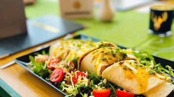 A meal with a wrap, salad, and a cup on a table with a view of mountains.