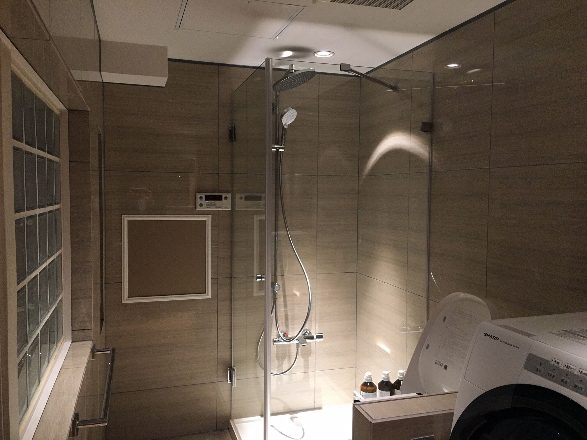 A modern bathroom with a glass-enclosed shower, a built-in toilet, and a washing machine.