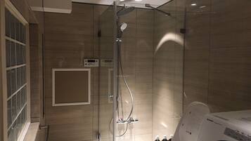 A modern bathroom with a glass-enclosed shower, a built-in toilet, and a washing machine.