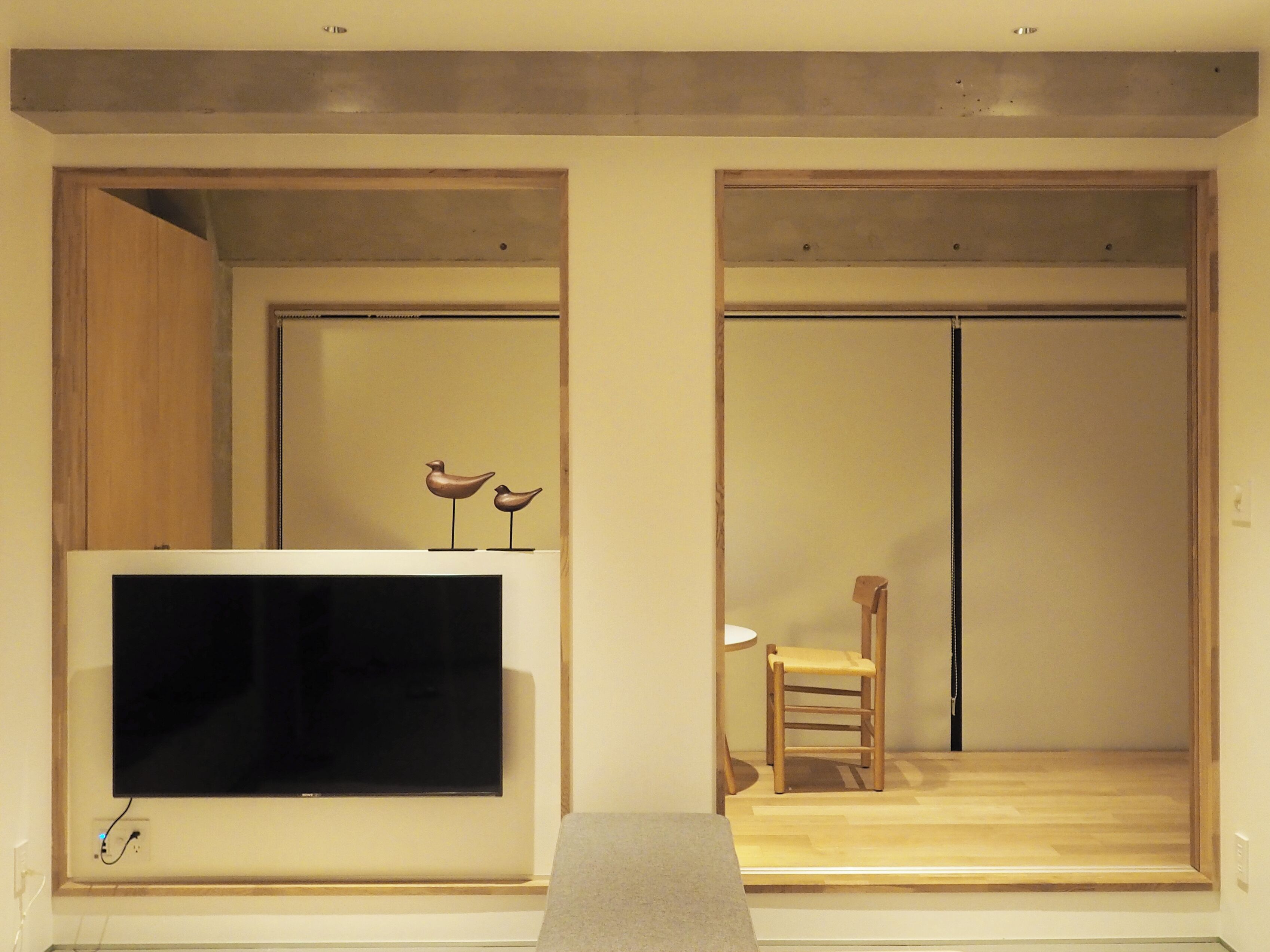 A room with a flat-screen TV mounted on a wall, a wooden chair, and a small table.
