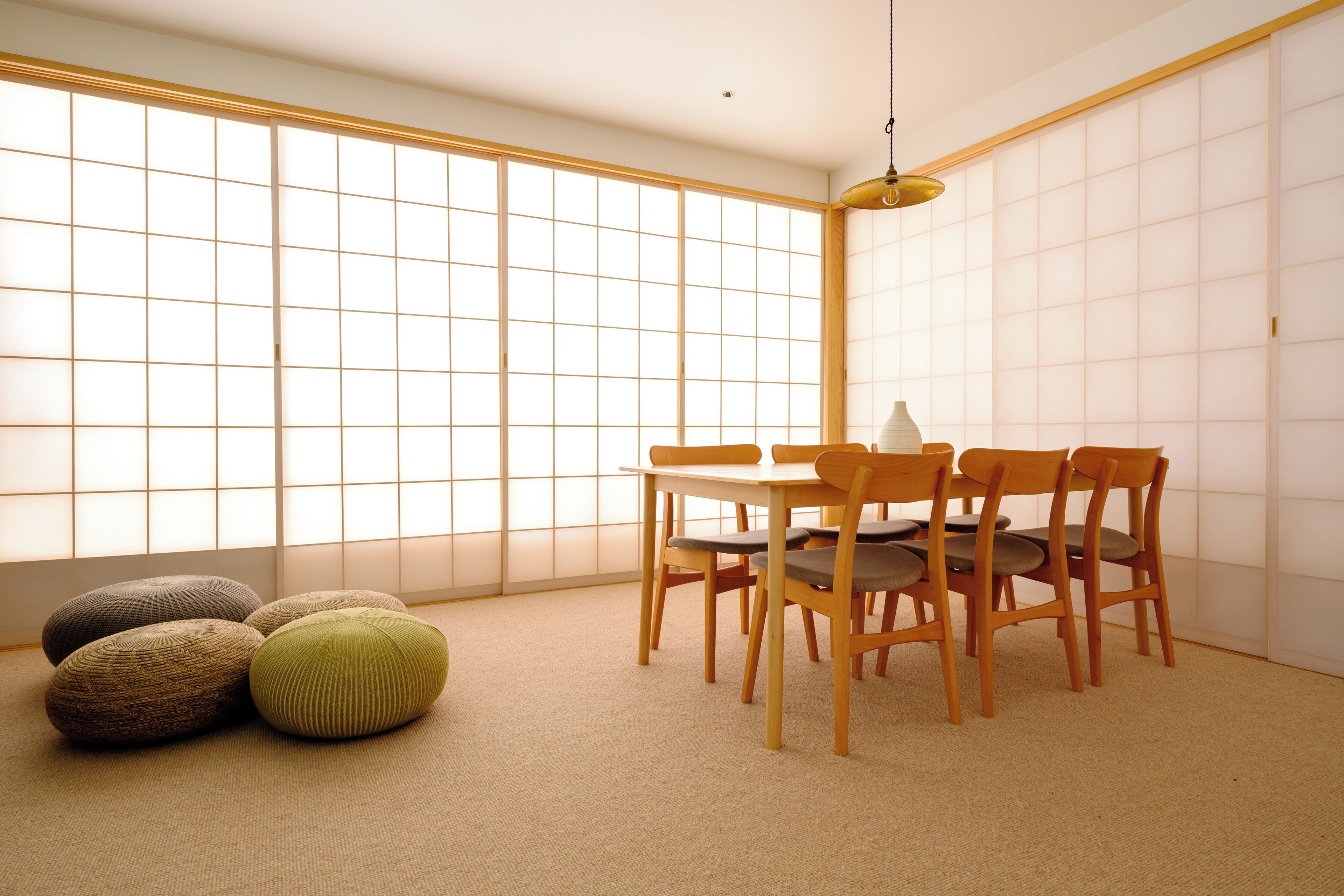 Um quarto japonês tradicional com tatames, uma mesa baixa com cadeiras de madeira e um painel de parede com portas shoji.