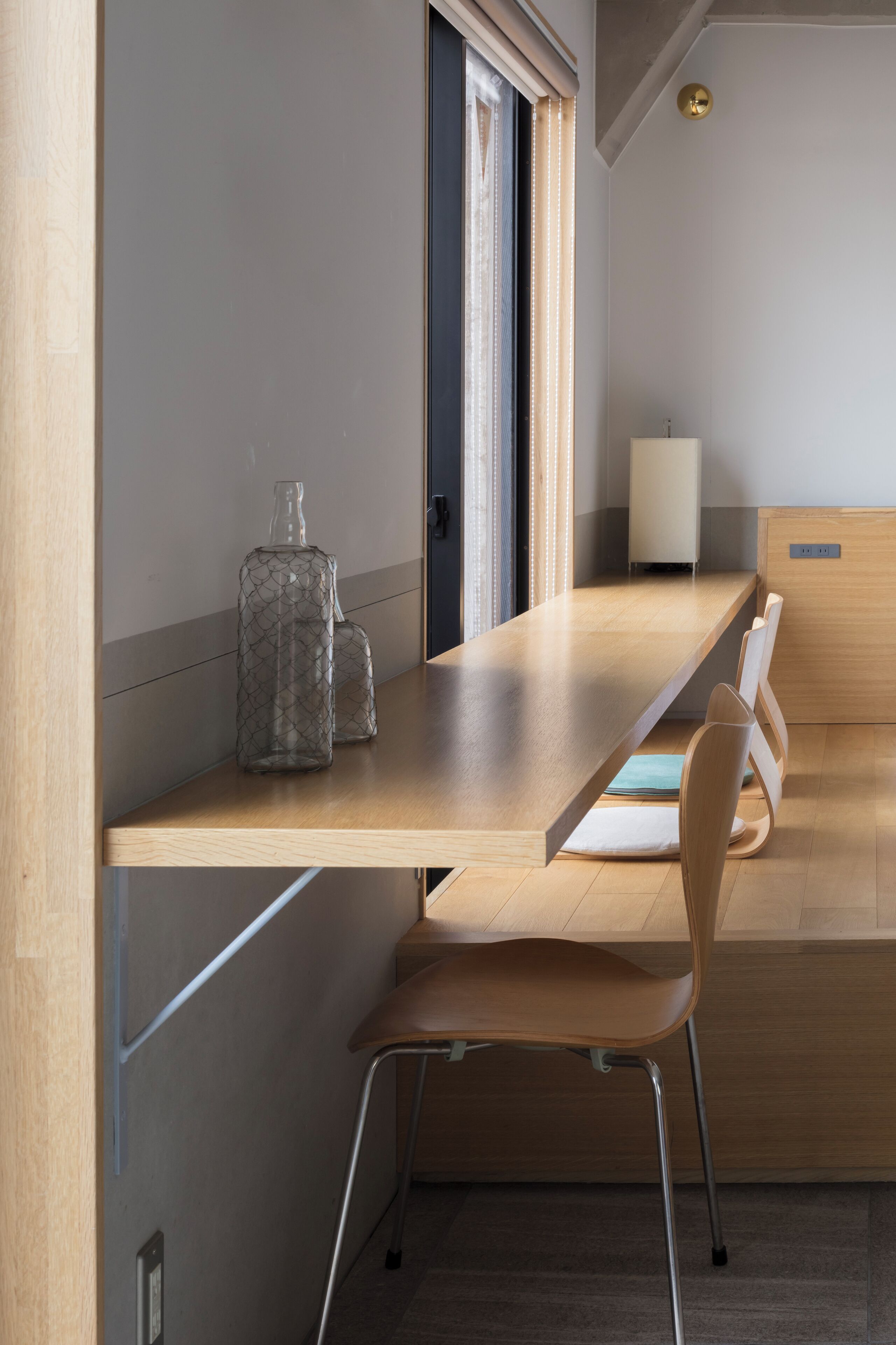 Una habitación moderna con un escritorio de madera, una silla y un ventanal con persianas.