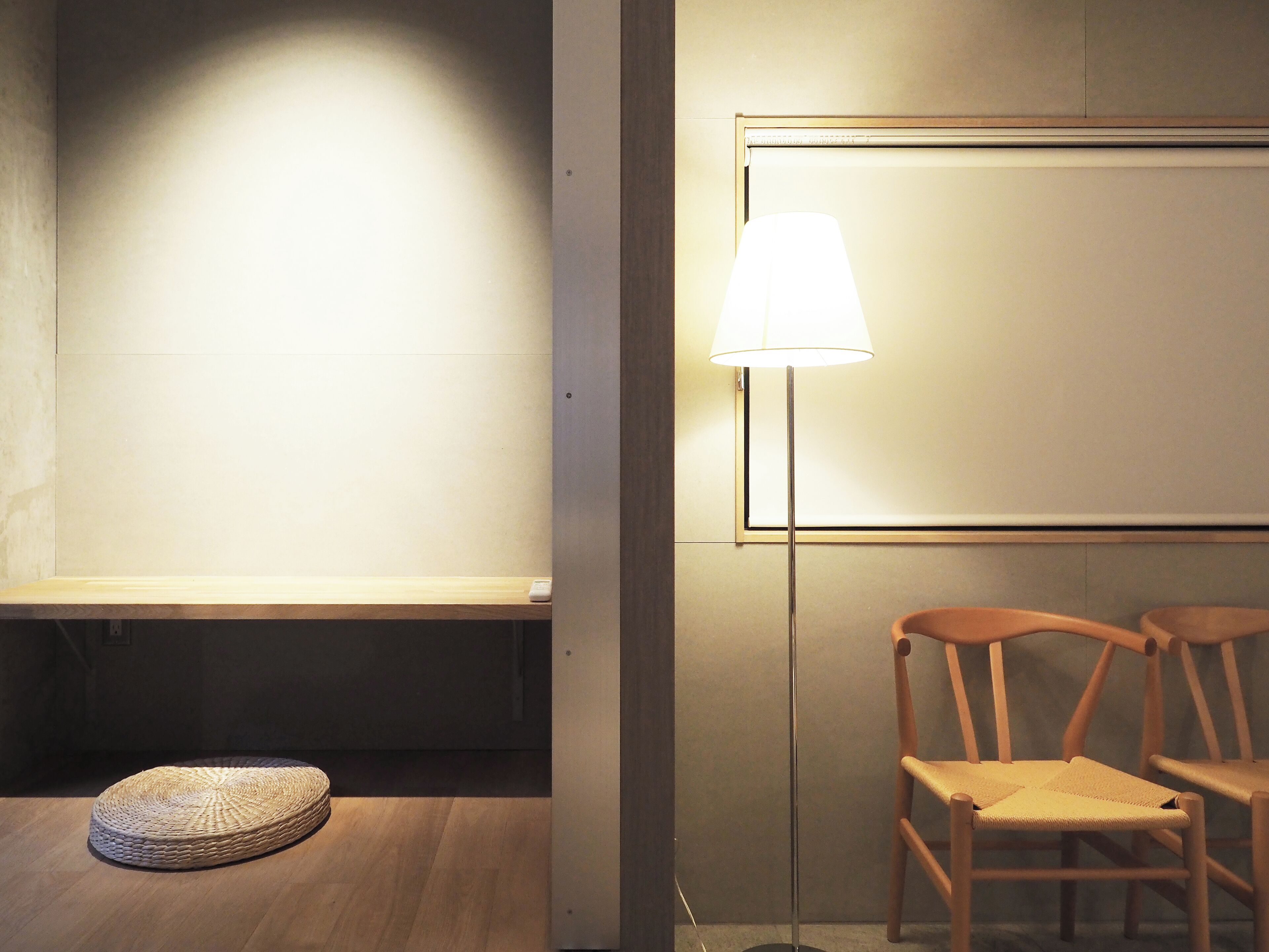 Habitación minimalista con un banco de madera, un pouf tejido y dos sillas de madera.
