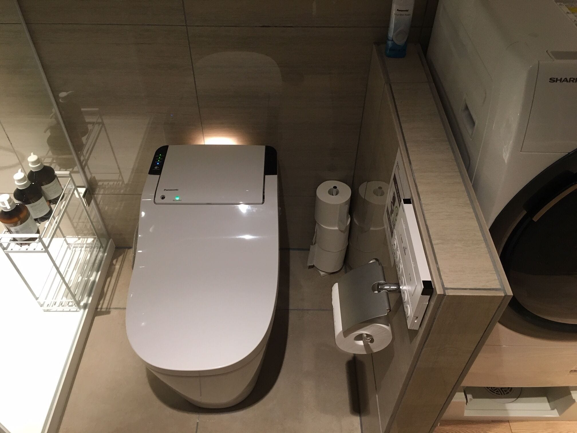 A modern bathroom with a toilet, toilet paper, and a paper towel dispenser.