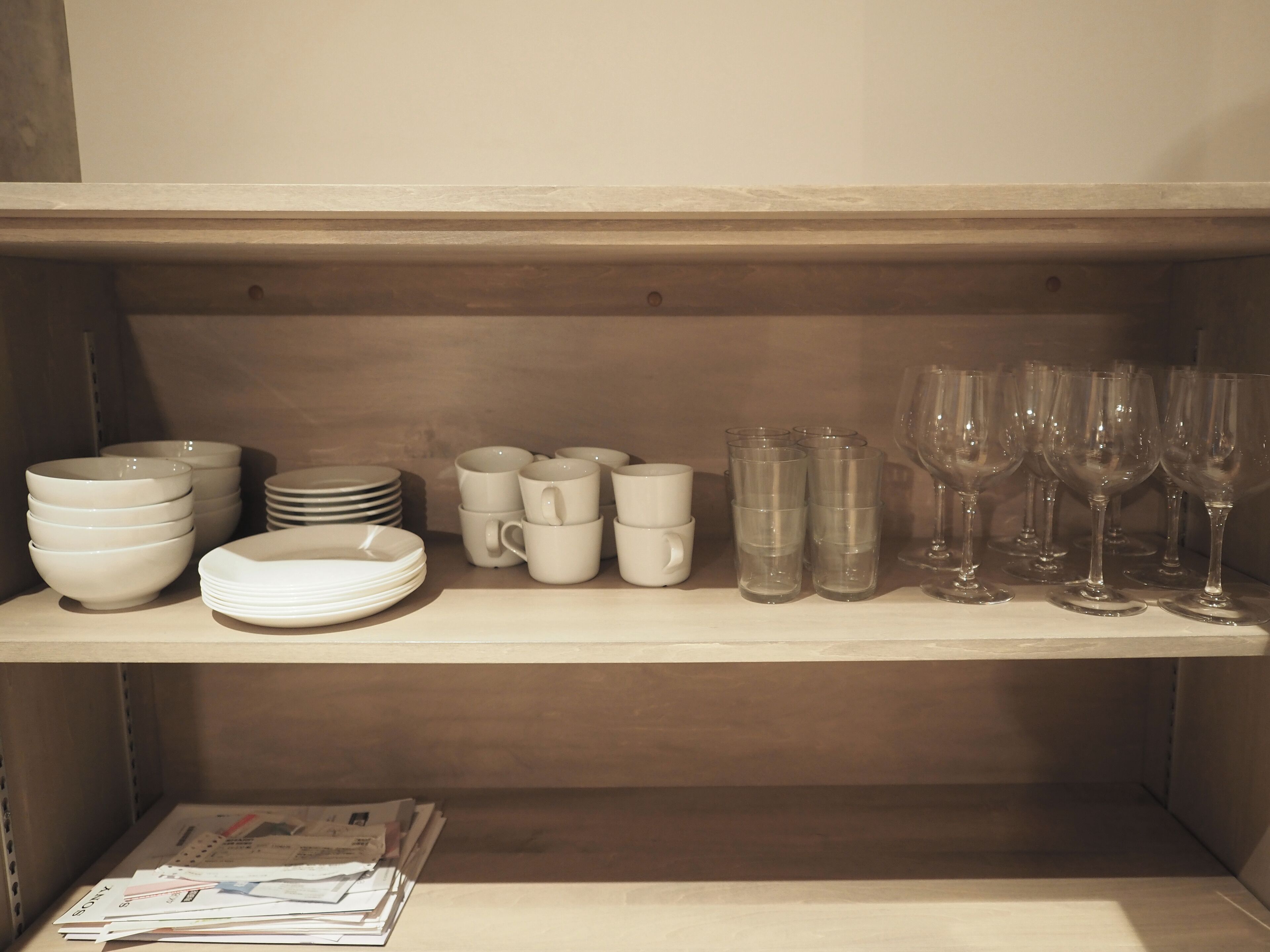 A shelf with stacked white bowls, plates, and clear glasses.