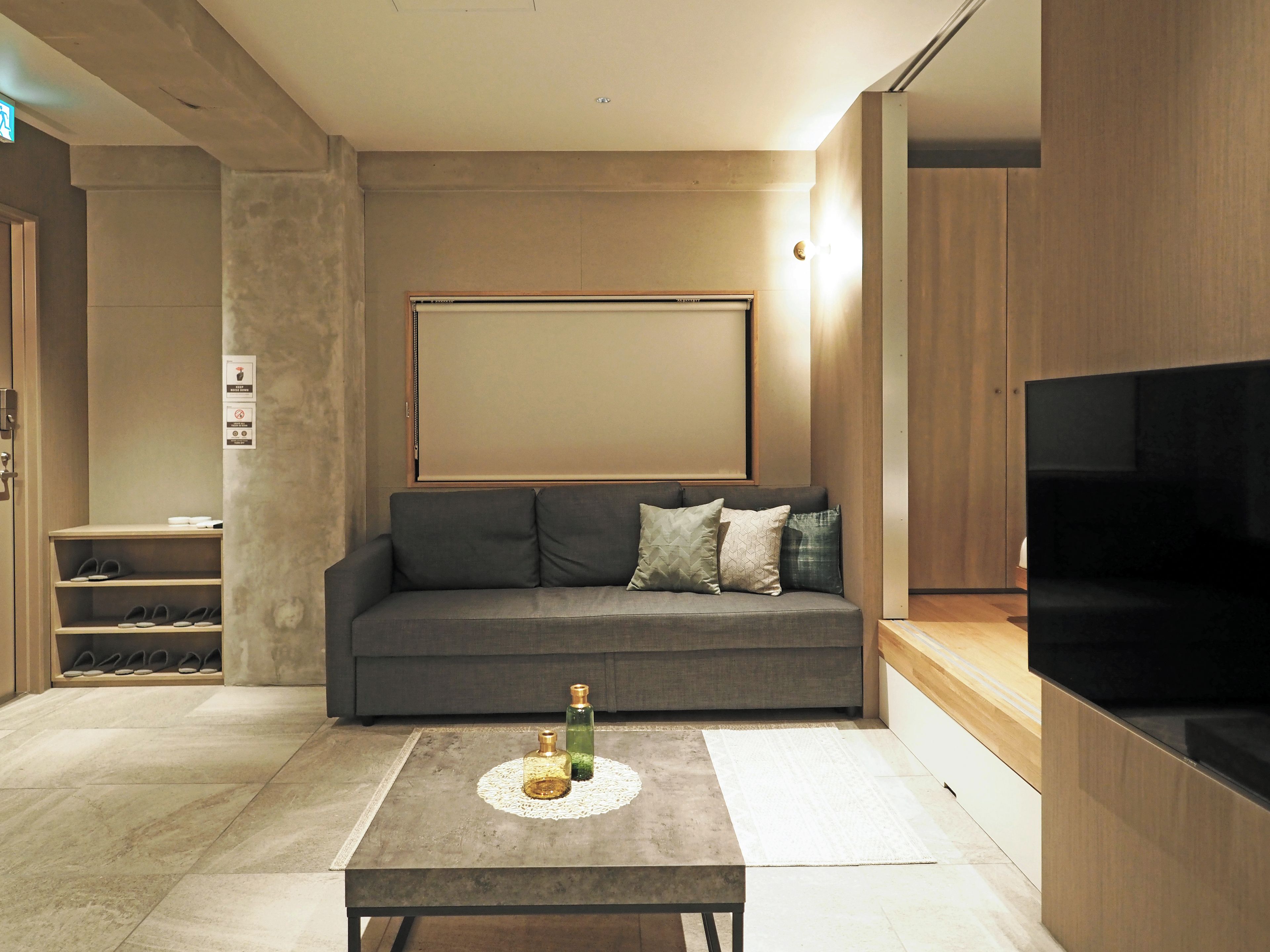 Una sala de estar moderna con un sofá gris, una mesa de centro con botellas decorativas, un televisor de pantalla plana y un mueble de madera.