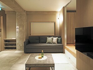 Una sala de estar moderna con un sofá gris, una mesa de centro con botellas decorativas, un televisor de pantalla plana y un mueble de madera.
