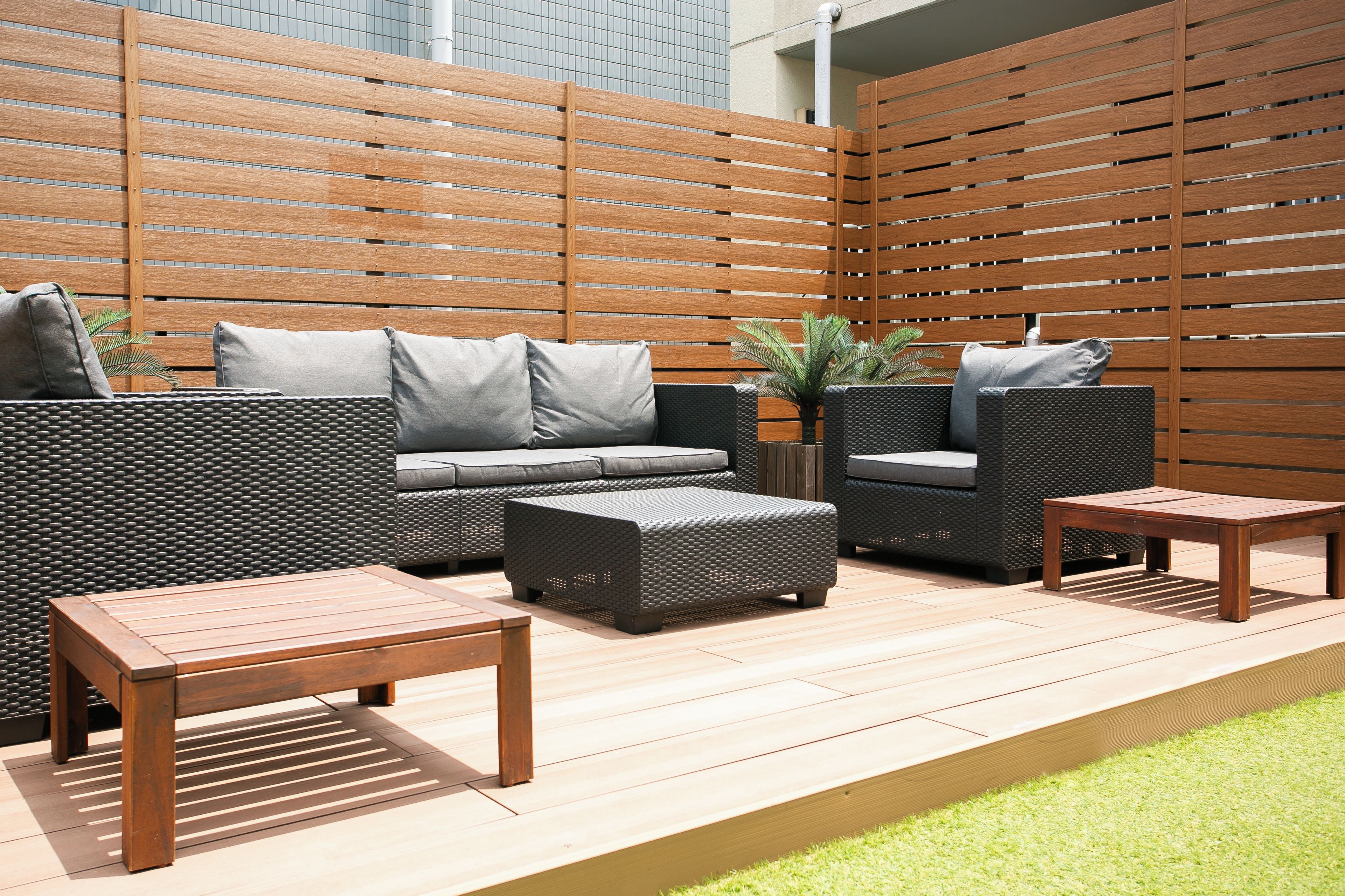 Een terras buiten met houten omheining, een zithoek, een kleine tafel en een plant in pot.