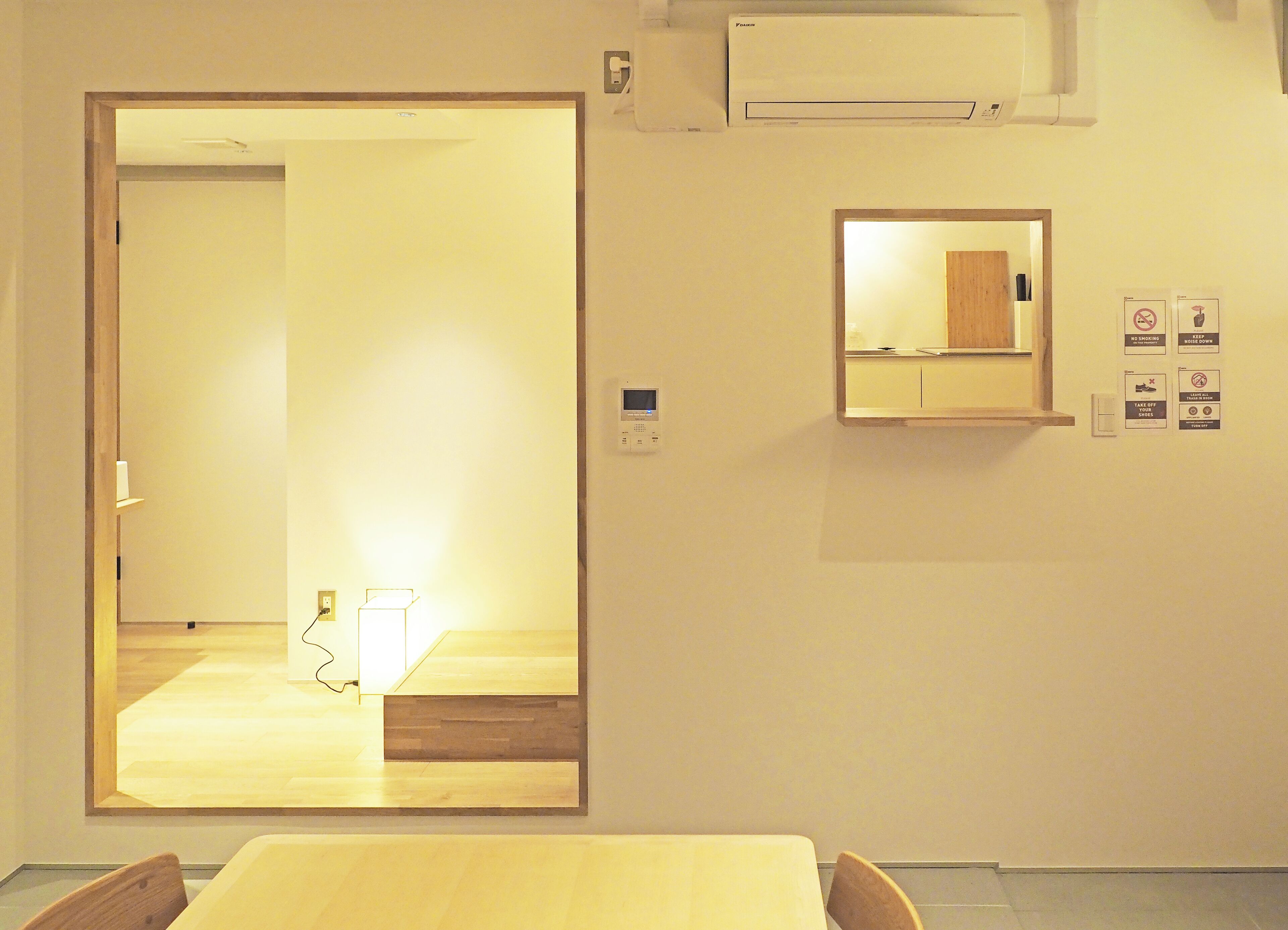 Quarto de hotel com piso de madeira, uma cama, uma pequena mesa, uma cadeira, um espelho e ar condicionado fixado na parede.
