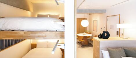 Una habitación de hotel moderna con una cama litera, una cama individual, un área de comedor y un baño.