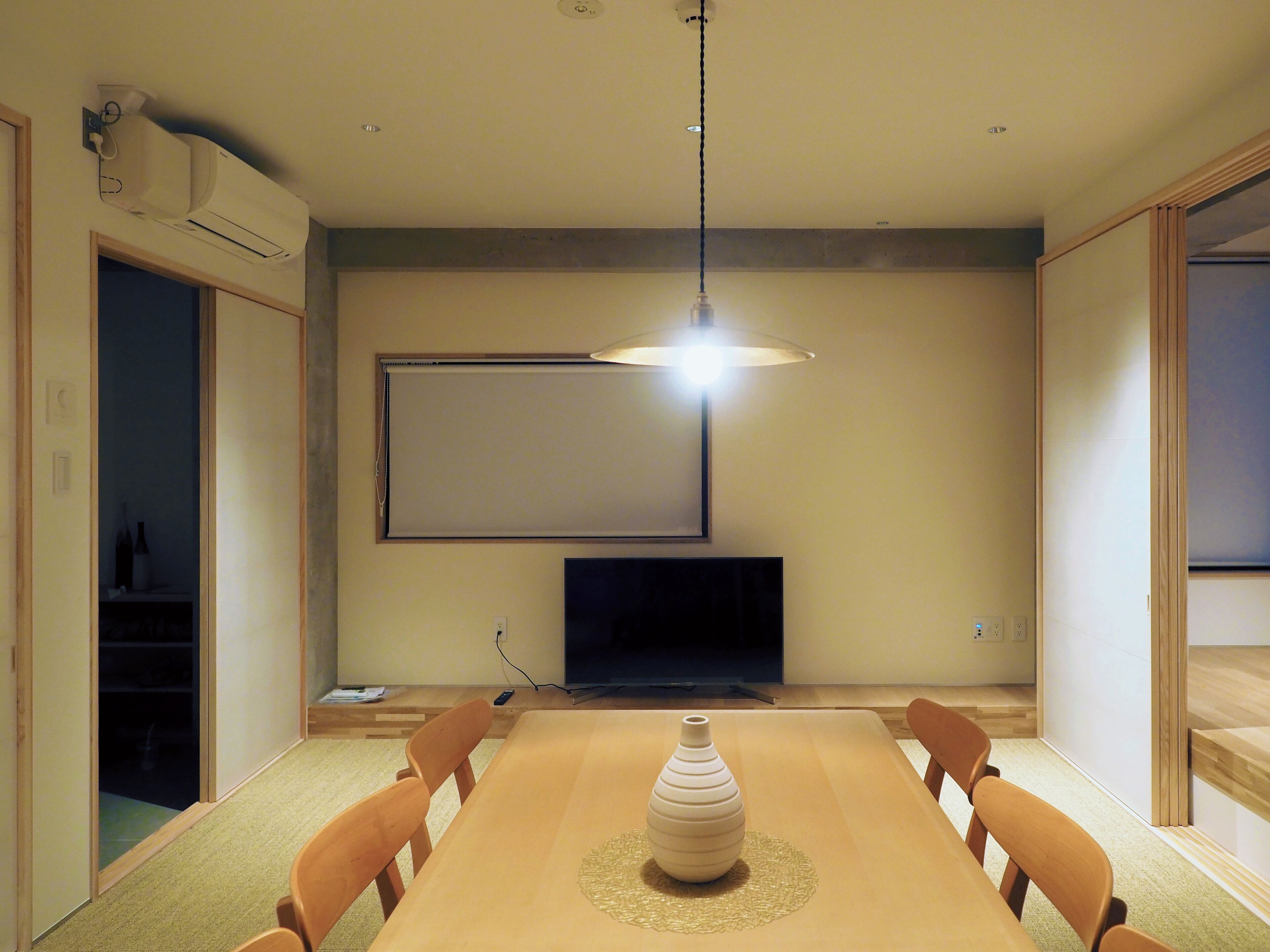 A dining area with a wooden table, chairs, a vase, a television, and a ceiling light.