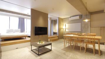 A modern hotel room with a bed, a TV, a dining area with chairs and a table, and a large window.