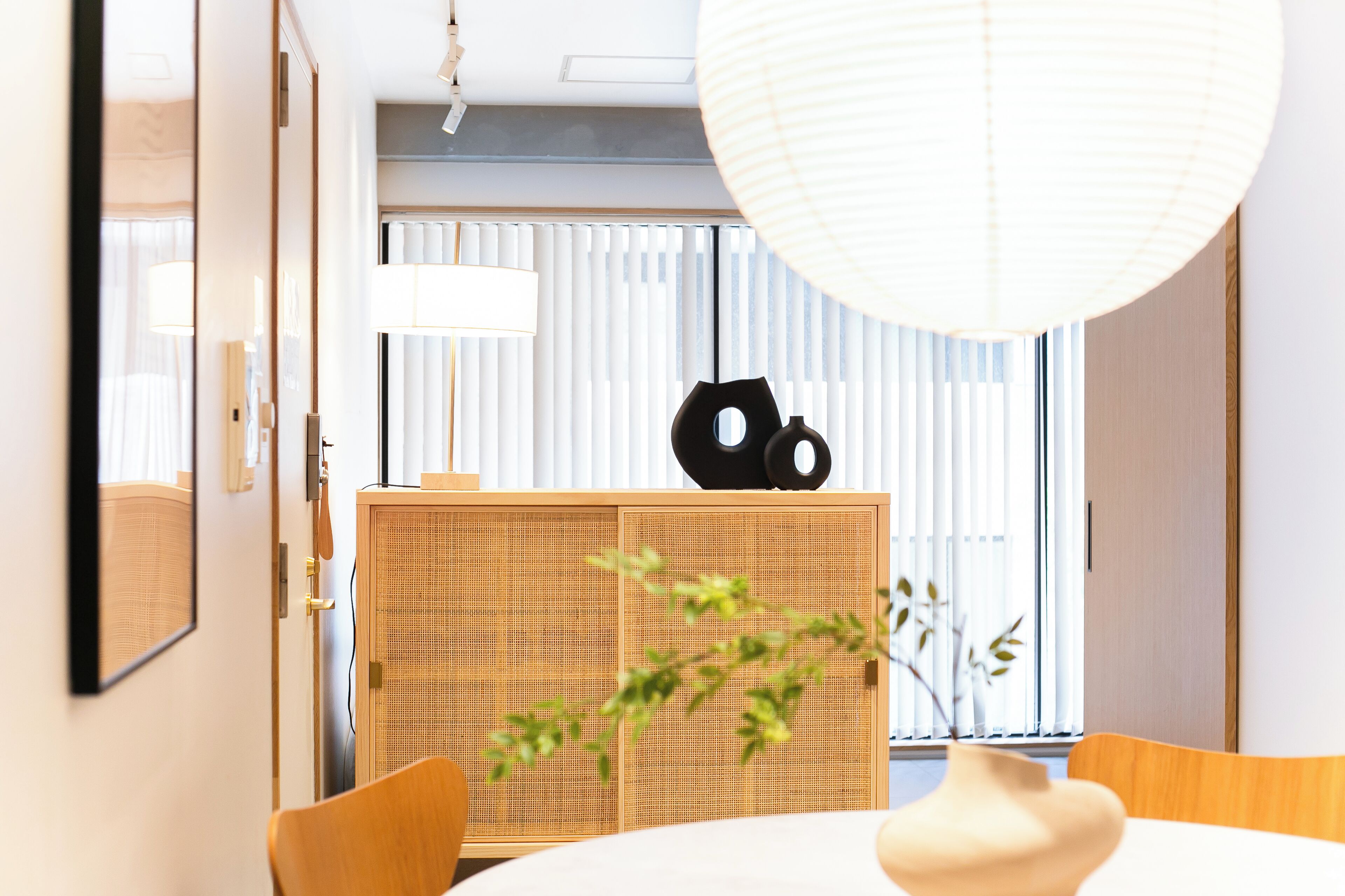 A modern hotel room with a wooden cabinet, a large hanging light fixture, and a view of the outside through sheer curtains.