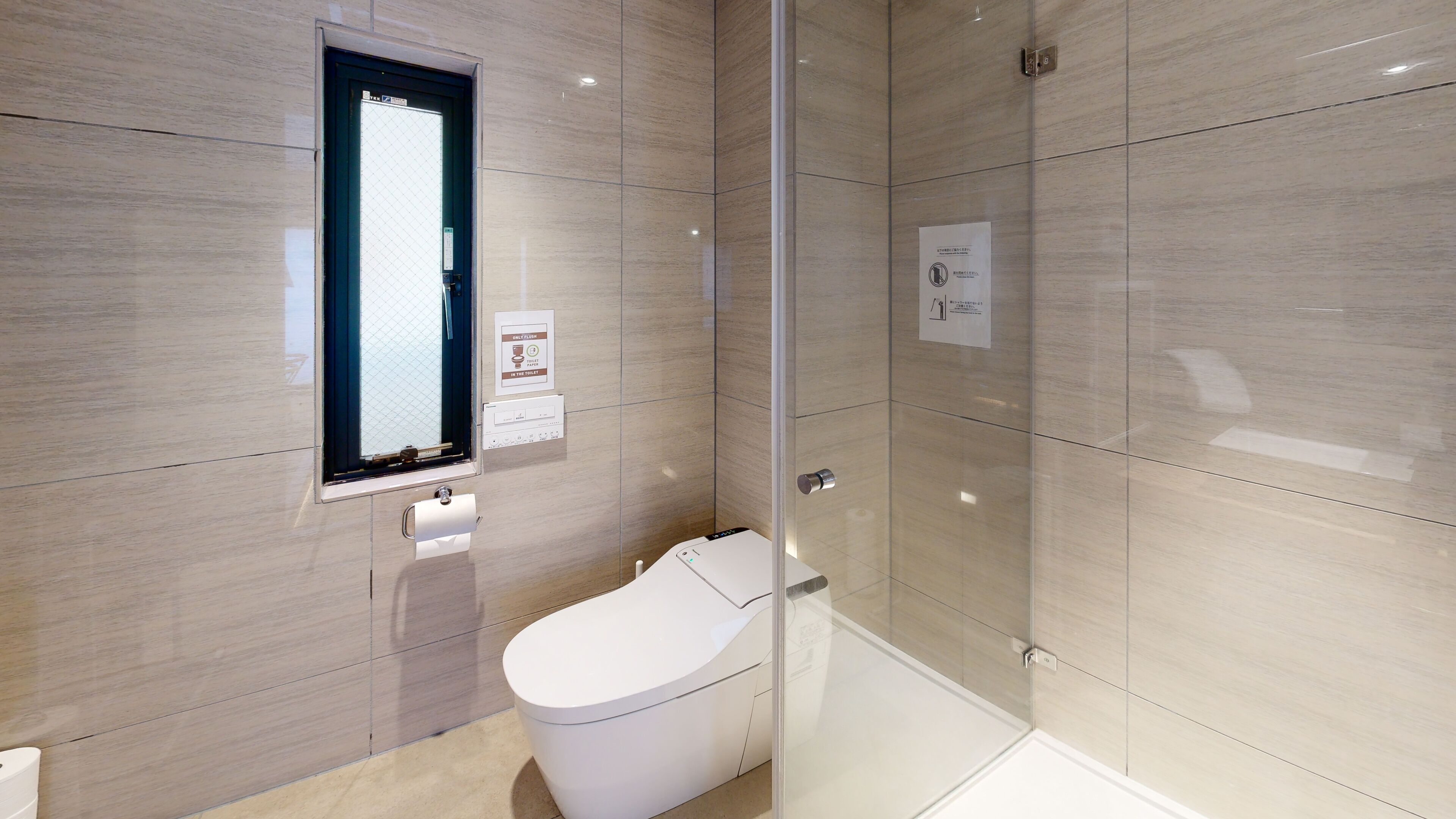Et moderne badeværelse med toilet, glasbrusekabine og hårtørrer.