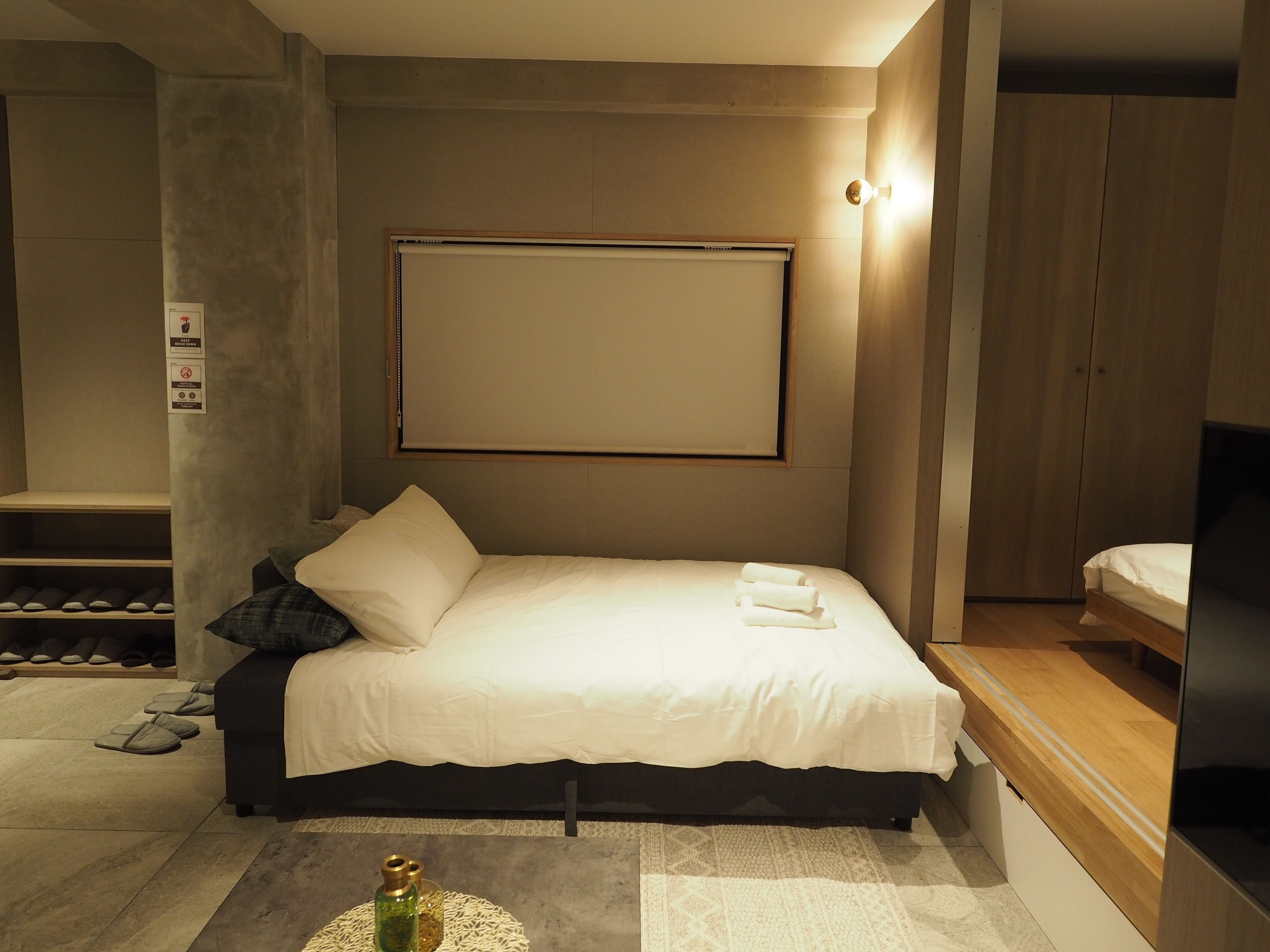 Un dormitorio moderno con cama, mesita de noche, armario de madera y televisor montado en la pared.