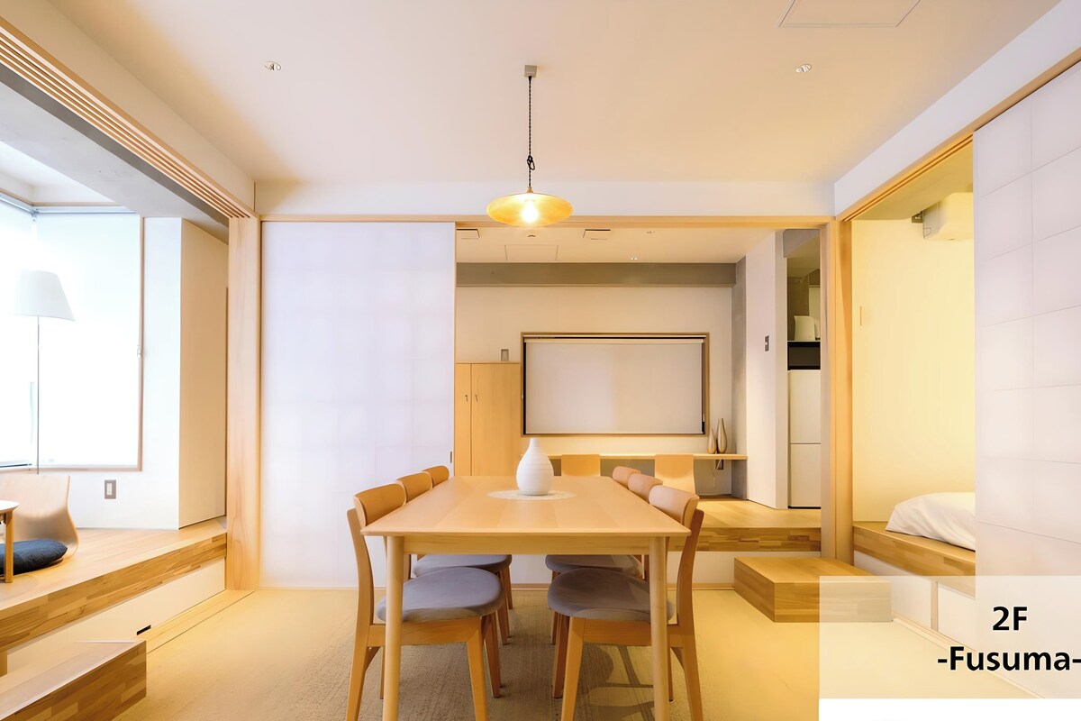 A modern, well-lit room with a wooden dining table, comfortable seating, and a large window providing natural light.