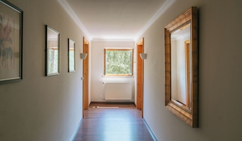 Um corredor com quadros nas paredes, uma janela com vista para árvores e um radiador no chão.