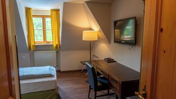 Ett hotellrum med en säng, ett skrivbord, en stol, en lampa, en tv och ett fönster med gardiner.