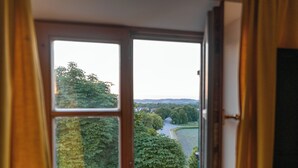 A room with a large window offering a view of a green landscape and a river. - Noon Mirch Hotel Restaurant (Eching)