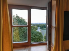 Quarto com uma grande janela que oferece vista para uma paisagem verde e um rio.