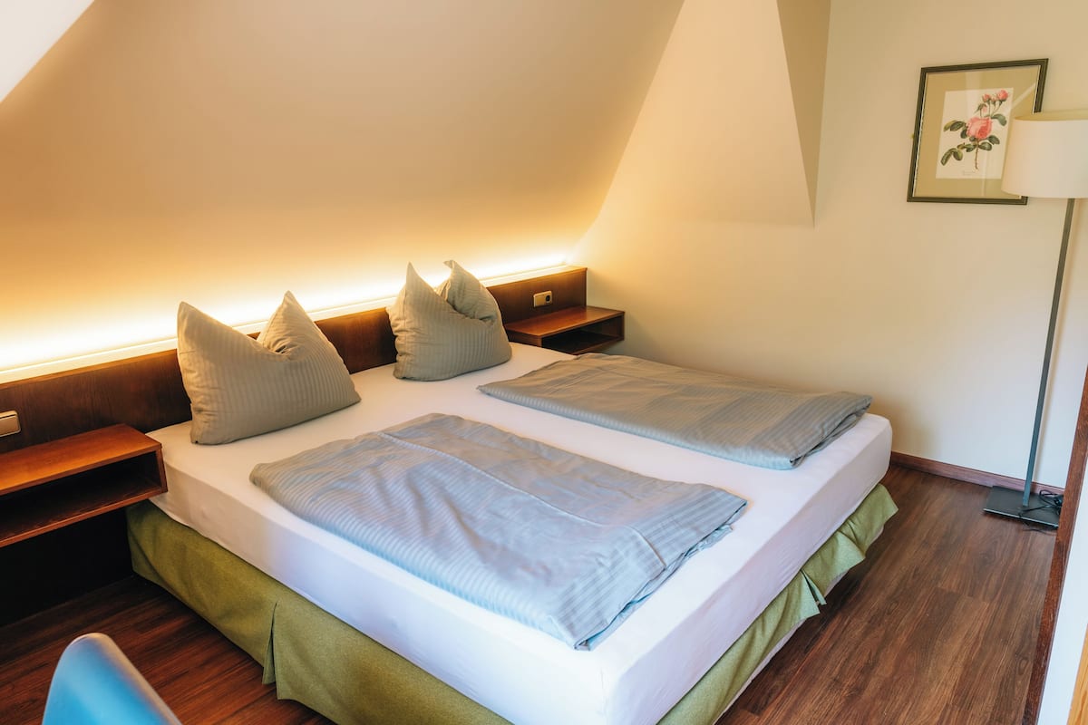 A neatly made twin bed with pillows, a bedside table, a lamp, and a framed picture on the wall.